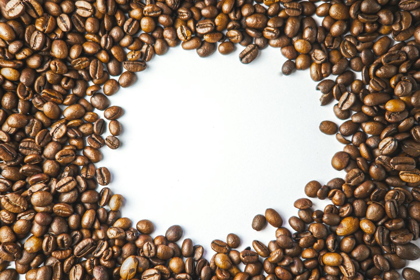 Geröstete Kaffeebohnen, die auf weißem Untergrund kreisförmig angeordnet sind.