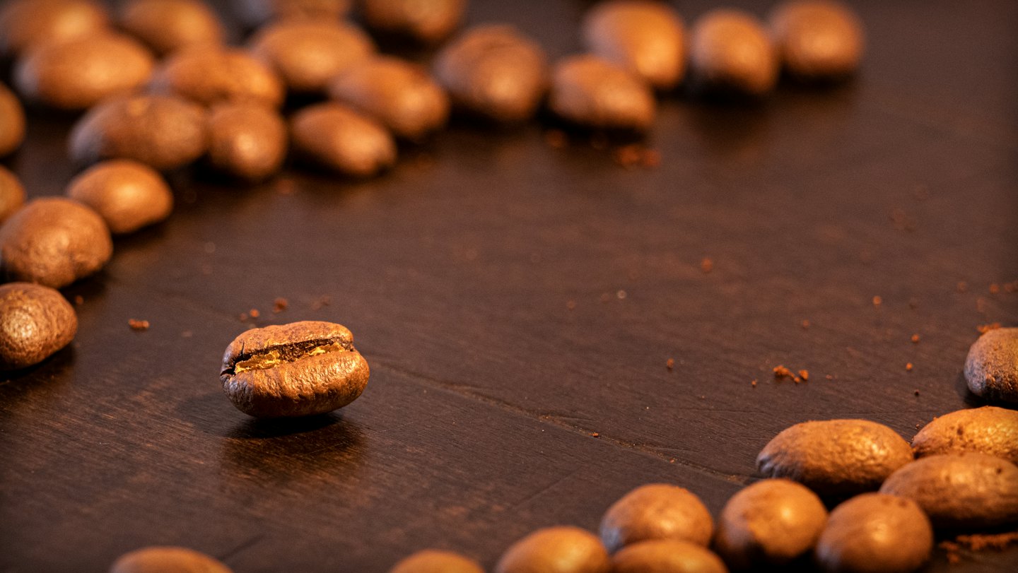 Geröstete Kaffeebohnen, die auf einer Holzoberfläche verstreut sind.